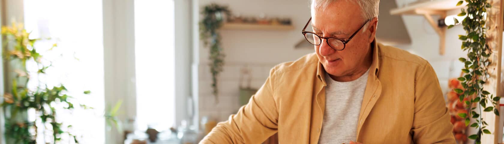 Senior Man Pouring Water In Glass While Having Breakfast At His Domestic Kitchen