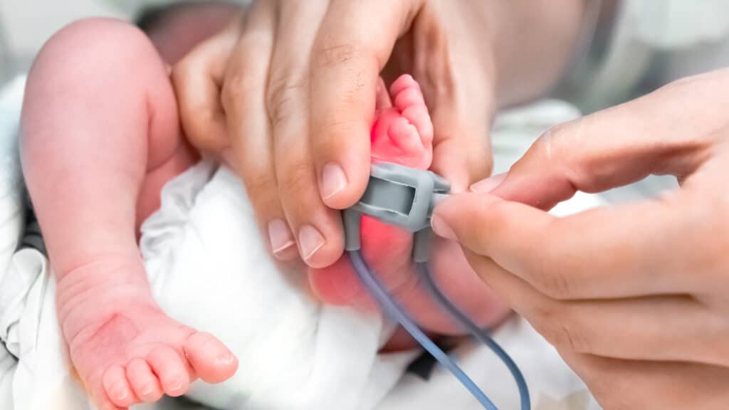 Nurse Is Putting On The Foot Of Neonatal Premature Infant Pulse Oximeter For Premature Babies, Selective Focus. Newborn Is Placed In The Incubator. Neonatal Intensive Care Unit